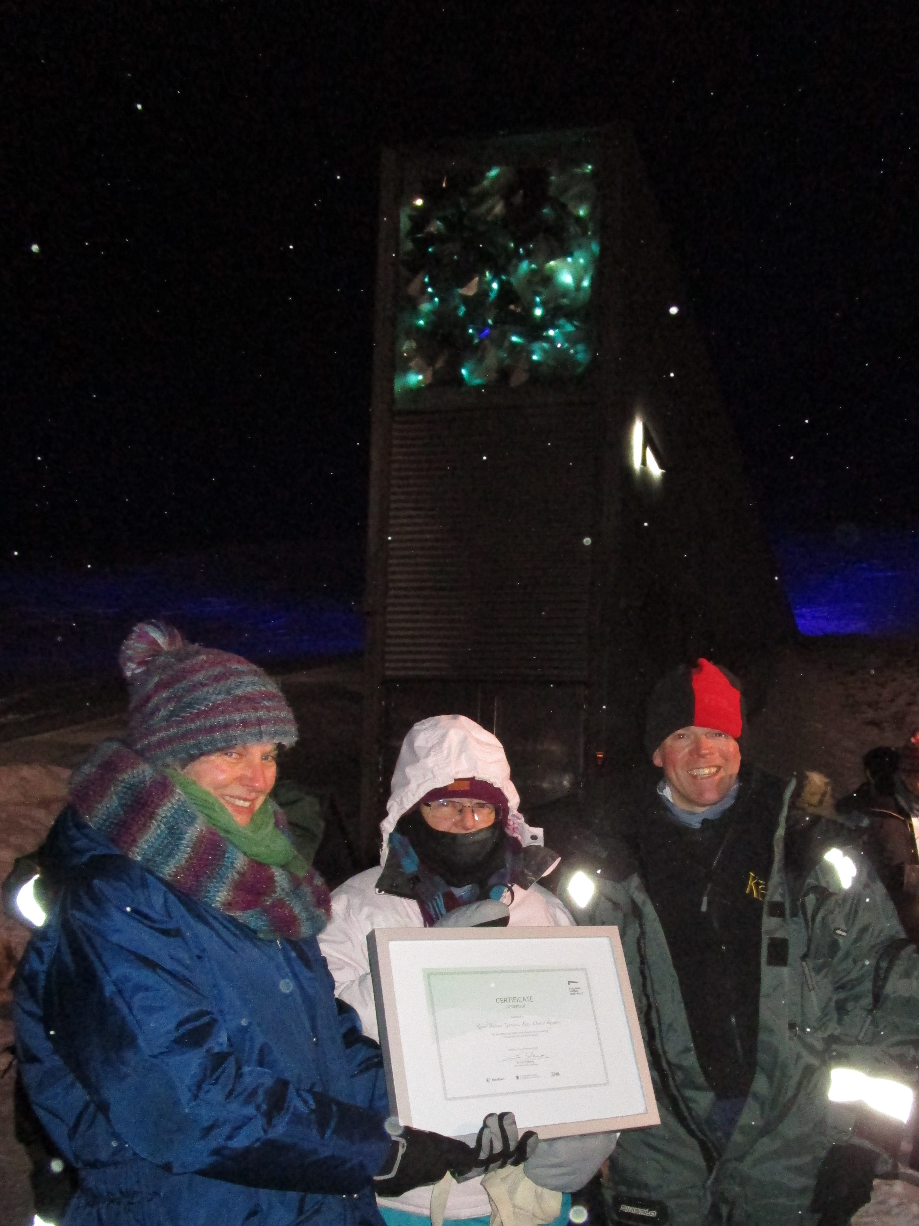 Three people stood holding a framed certificate infront of the Svalbard Global Seed Vault.